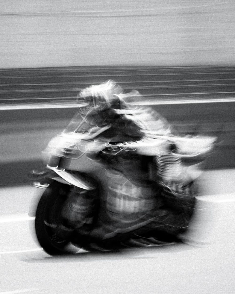 Motociclista inclinado em alta velocidade, com o corpo e a pista borrados pelo movimento